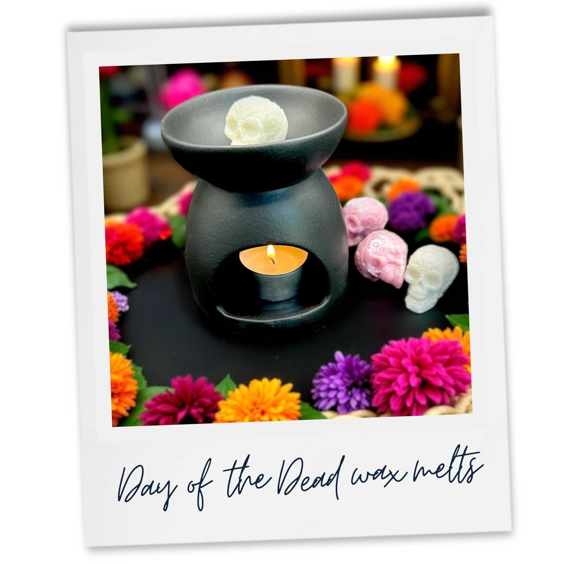 Day of the Dead skull wax melt in black wax burner surrounded by colourful flowers and skull-shaped wax melts on a blurred background.
