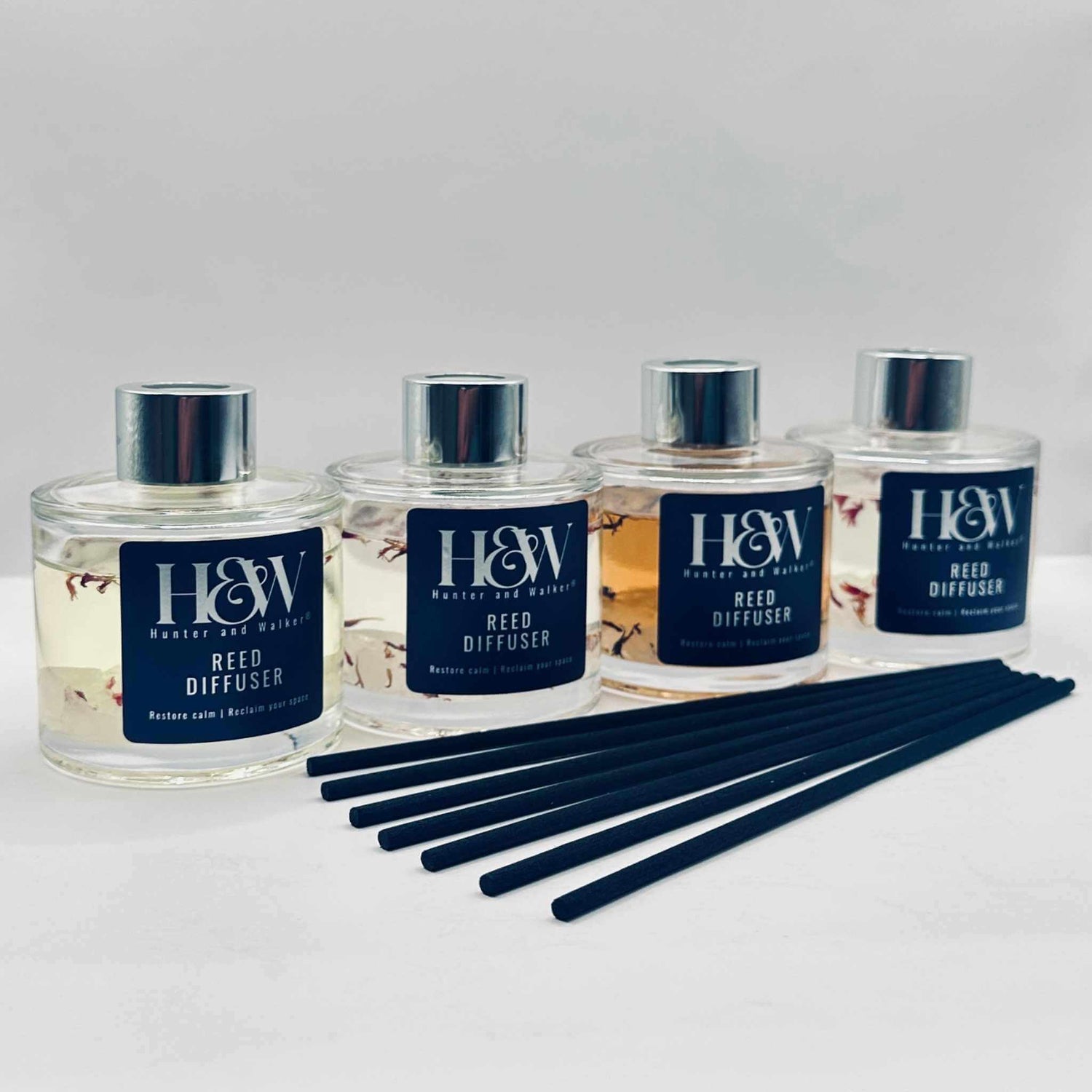Four Luxury reed diffusers in a row with black reeds on a white background