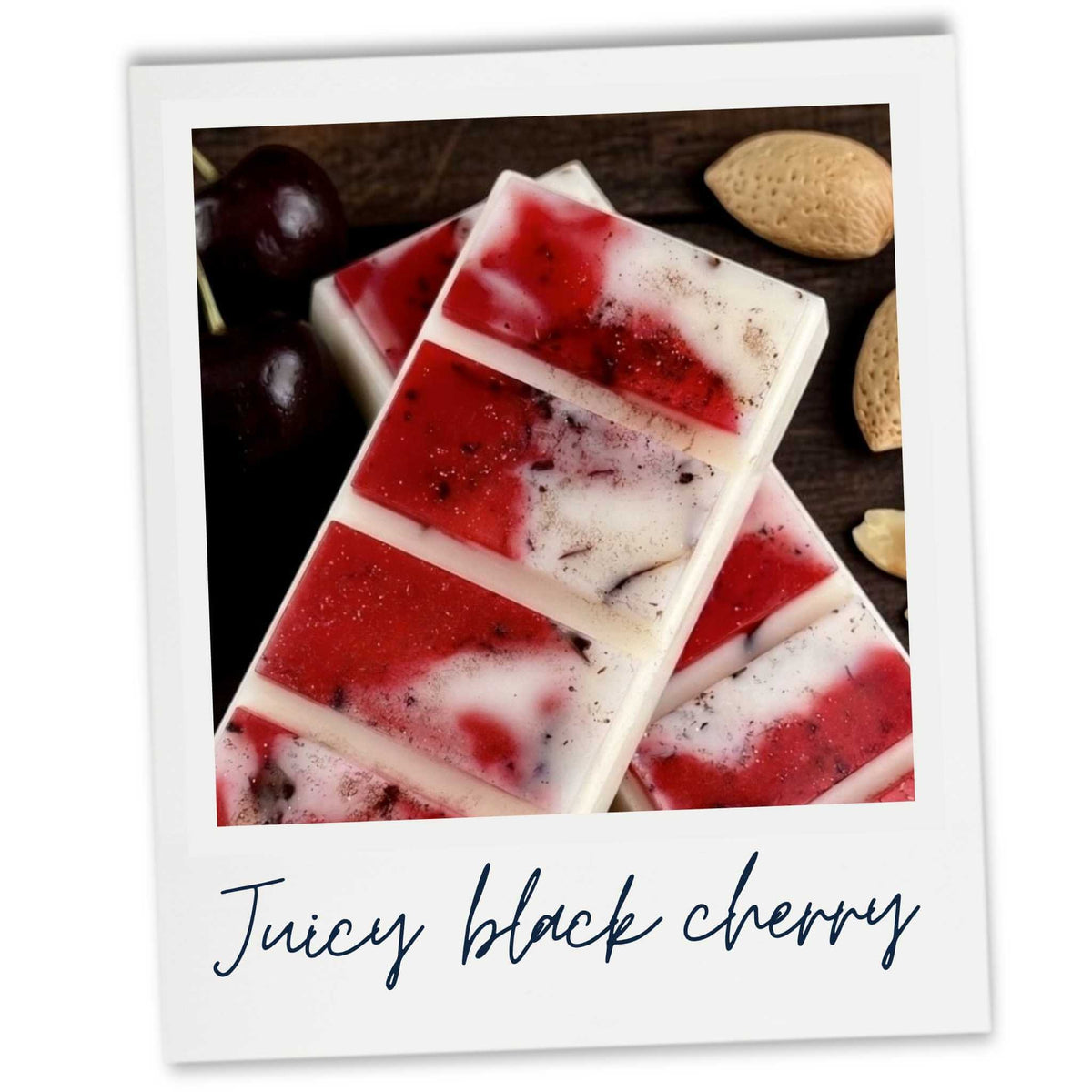 A Polaroid-style photo showing Black Cherry Wax Melts designed with a red and white marbled pattern, with dark cherries and almond shells around them. The printed photo has a white border and the text 'Juicy black cherry' written below.