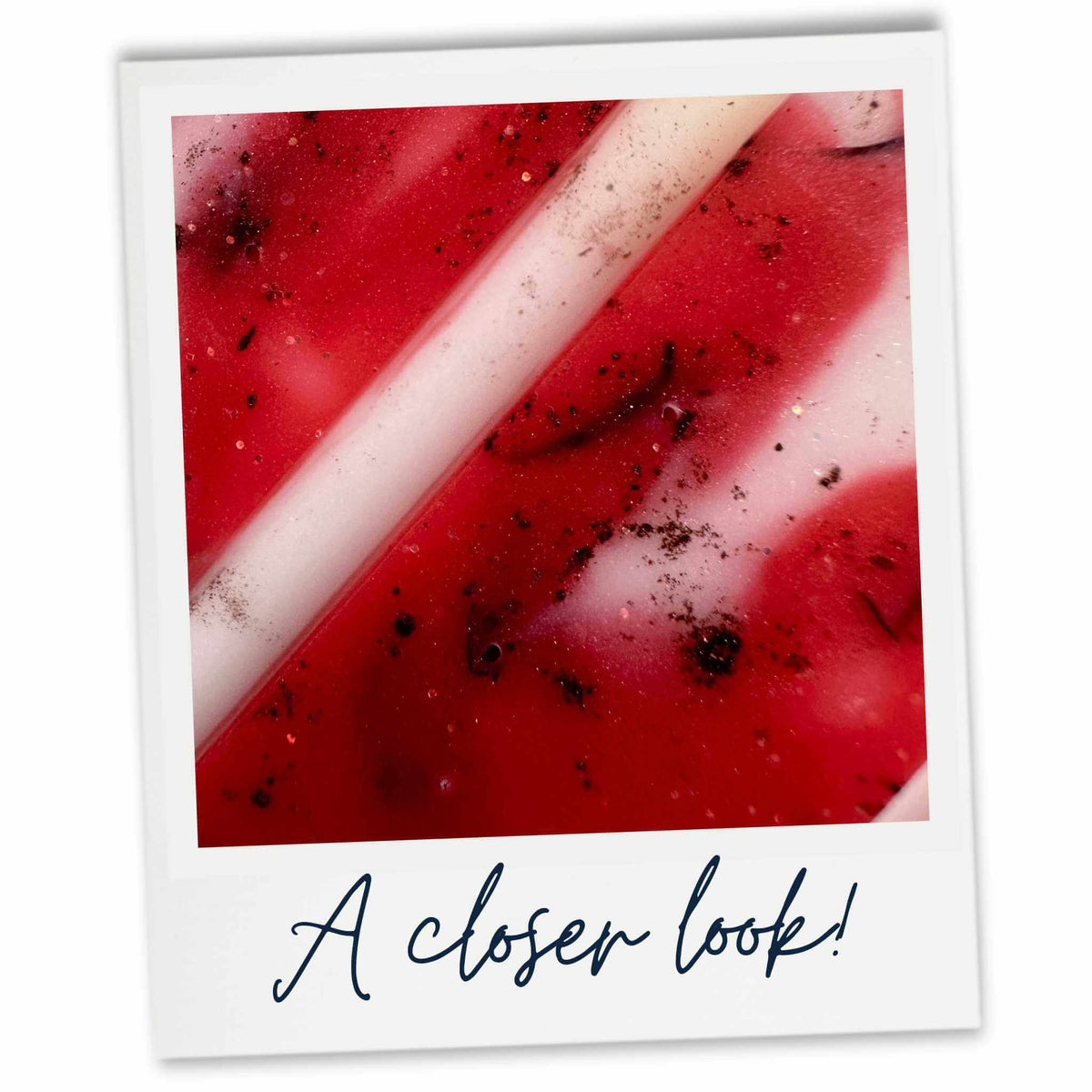 A close-up view inside a Polaroid-style photo frame showing a pinky red wax melt with white diagonal stripes and dark specks, with the text 'A closer look!' written below.