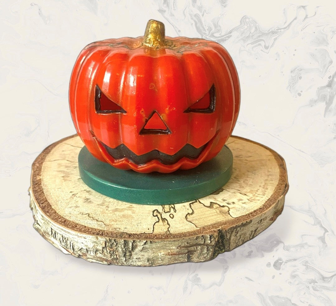 Orange wax pumpkin sat on a green base with log slice.