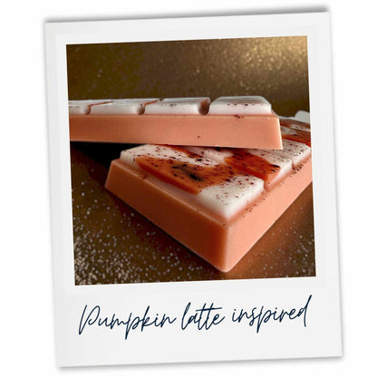 A square product photo of layered pumpkin latte-inspired wax melt bars, styled like a Polaroid print with a white border and the text 'Pumpkin latte inspired' at the bottom. The bars feature a latte coffee coloured base, white cream-like top layers, and pumpkin pie drizzle effect with a sprinkle of cinnamon and spices.
