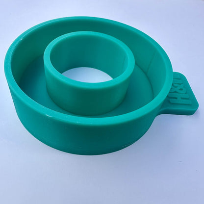 A side view of a teal green silicone ring shaped mold shown on a plain light background.