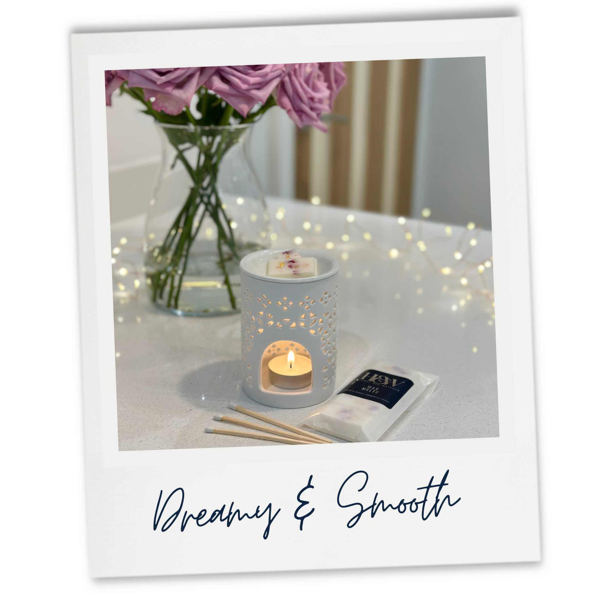 Velvet Santal wax melts in a white burner on a white worktop with a vase of pink flowers