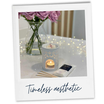 A White wax burner with lit candle, flowers, and wax melt on a counter top with 'Timeless aesthetic' text.